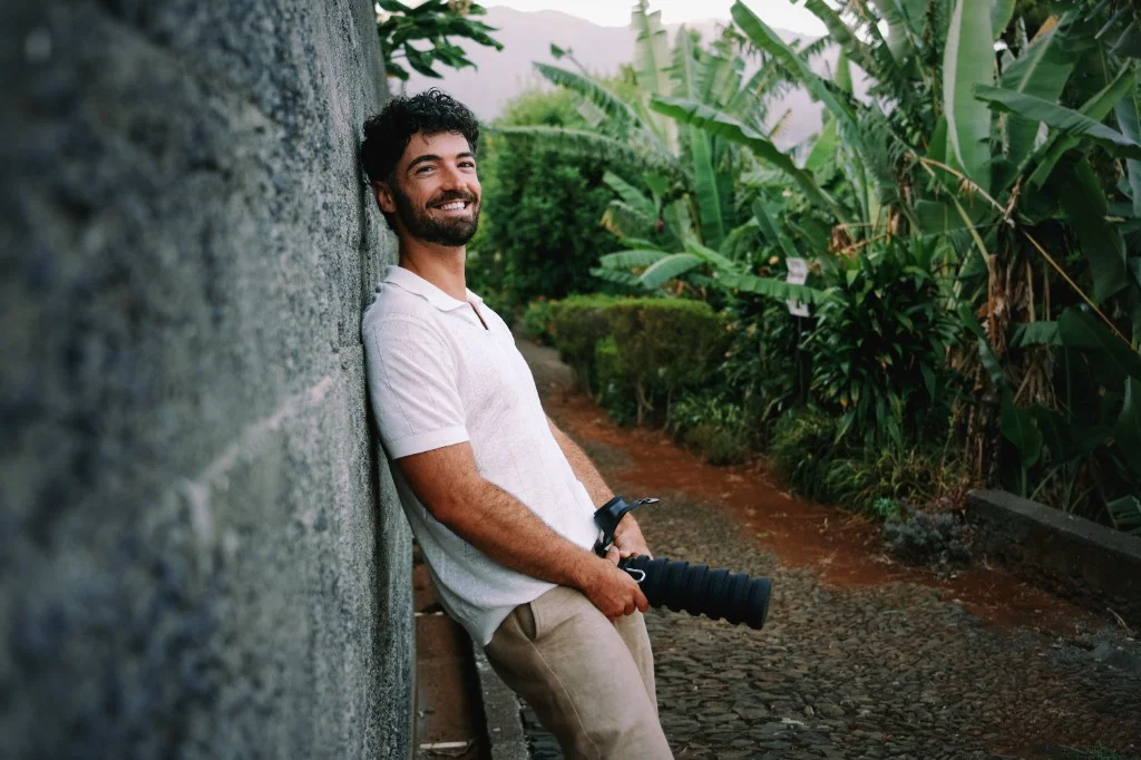 Henry Snow smiling while holding a camera in a tropical garden