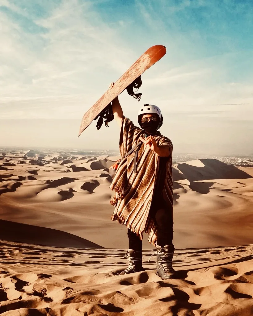 Igor Kondrat sandboarding on the dunes of Huacachina, Peru, holding a sandboard above his head